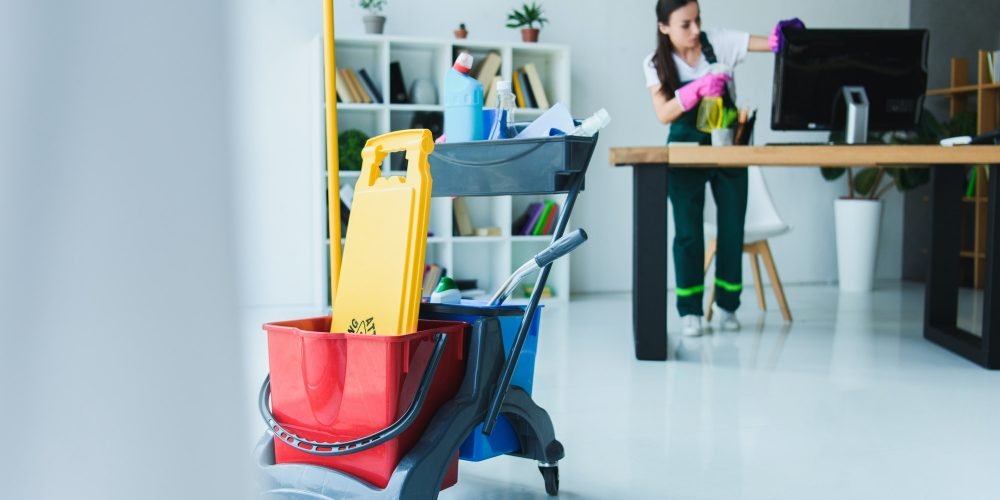 young-female-janitor-cleaning-office-with-various-cleaning-equipment.jpg